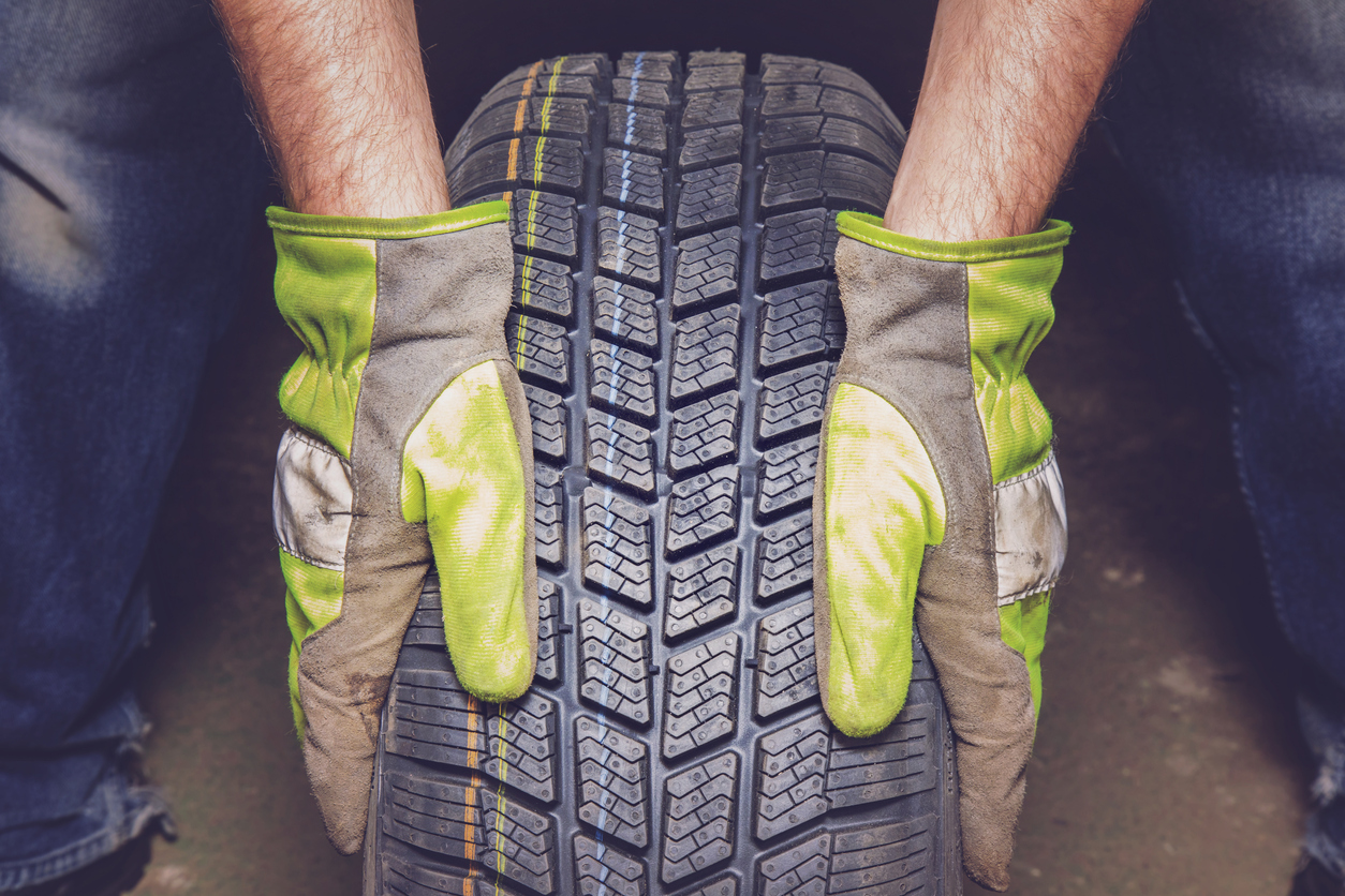 Man Holding New, Black Rubber Tire In The Garage.